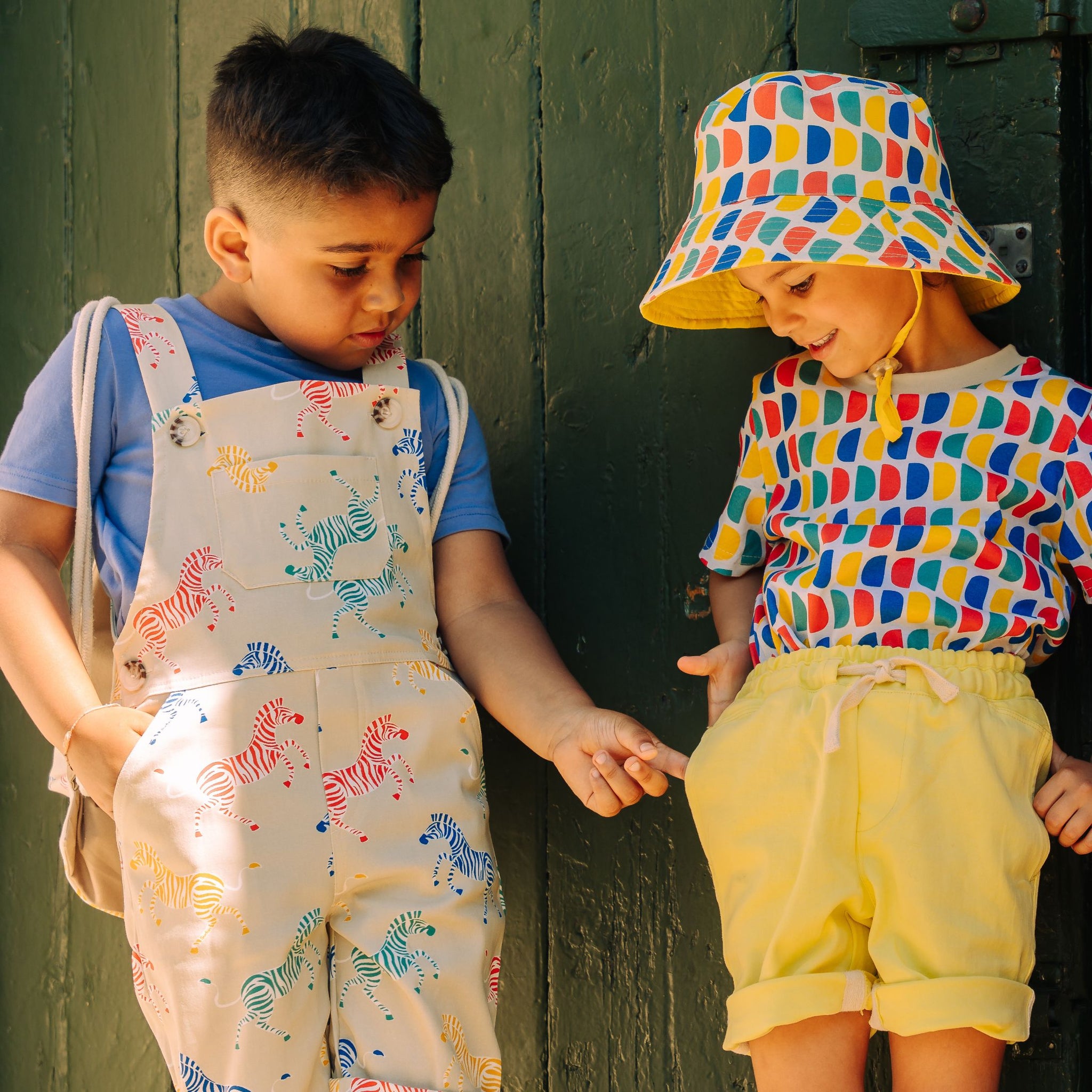 Two children standing side by side wearing bright summer clothes and looking for pockets