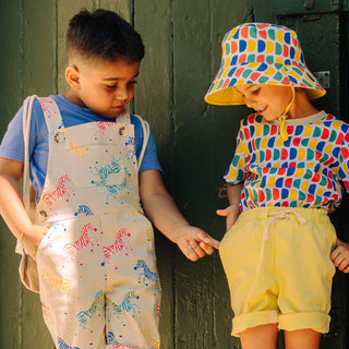Two children standing side by side wearing bright summer clothes and looking for pockets