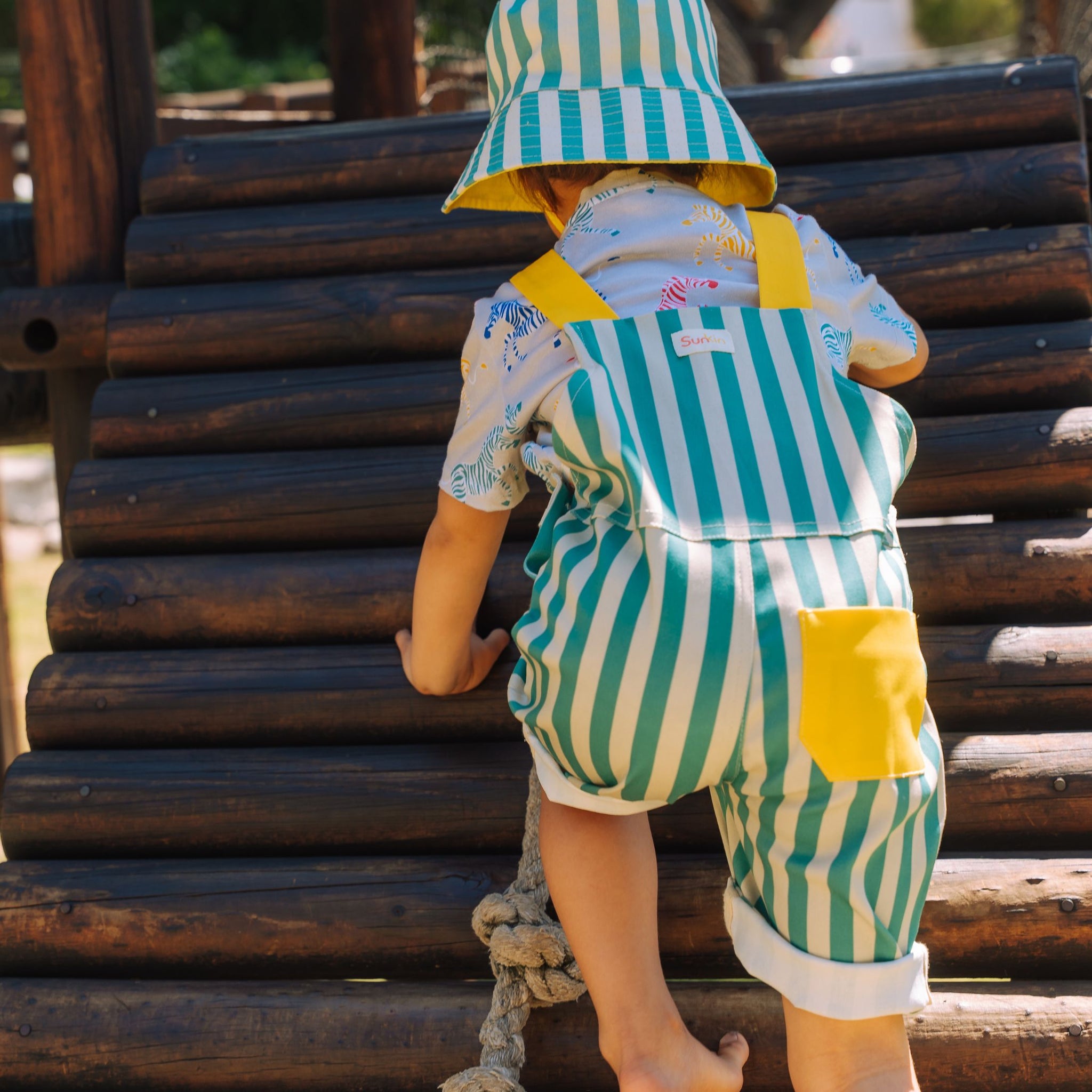 Toddler in the park climbing wearing green striped shortarees by SunKin