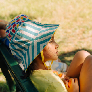 Child sitting on bench wearing SunKin green striped sun hat