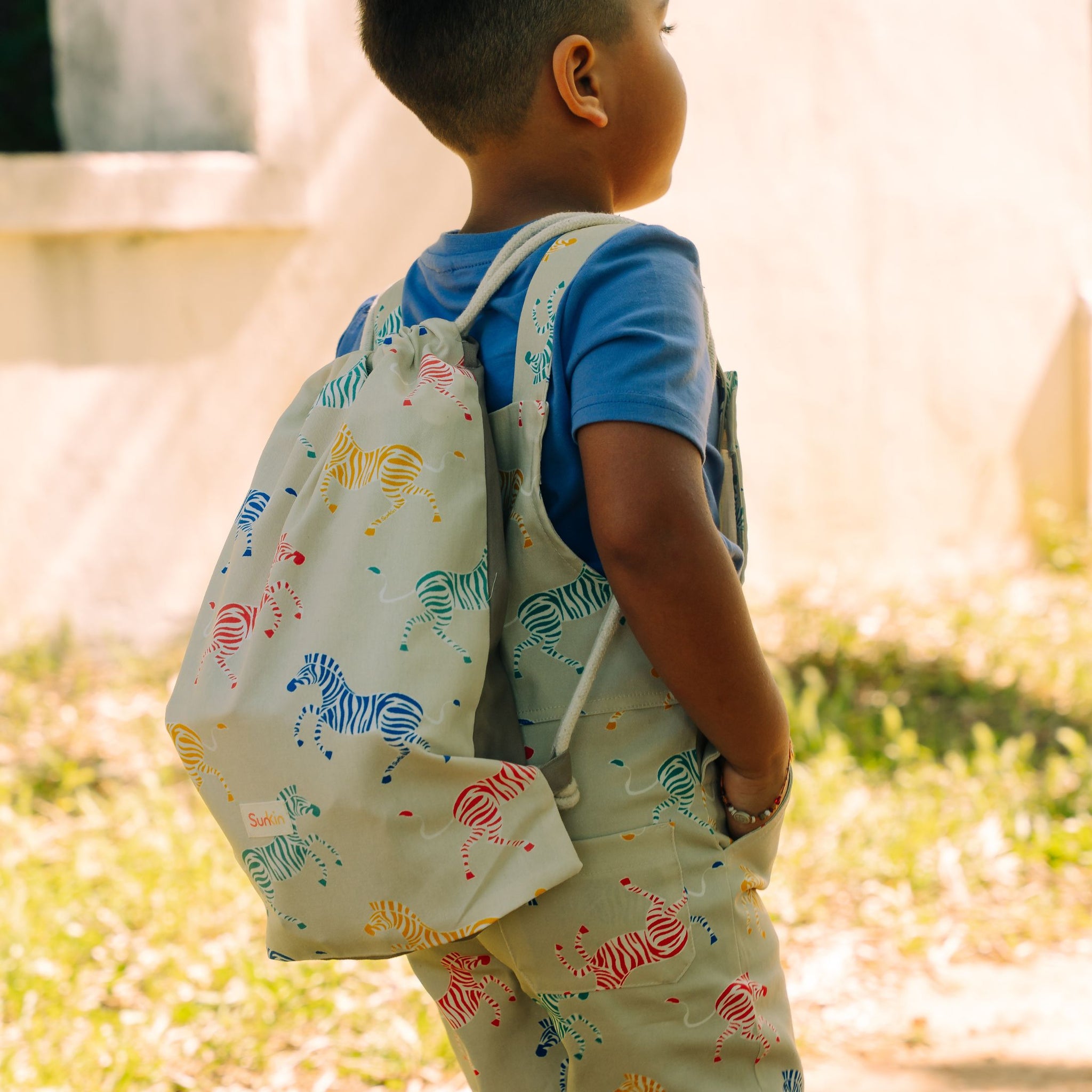 Boy wearing drawstring bag on back matching his overalls on a sunny day