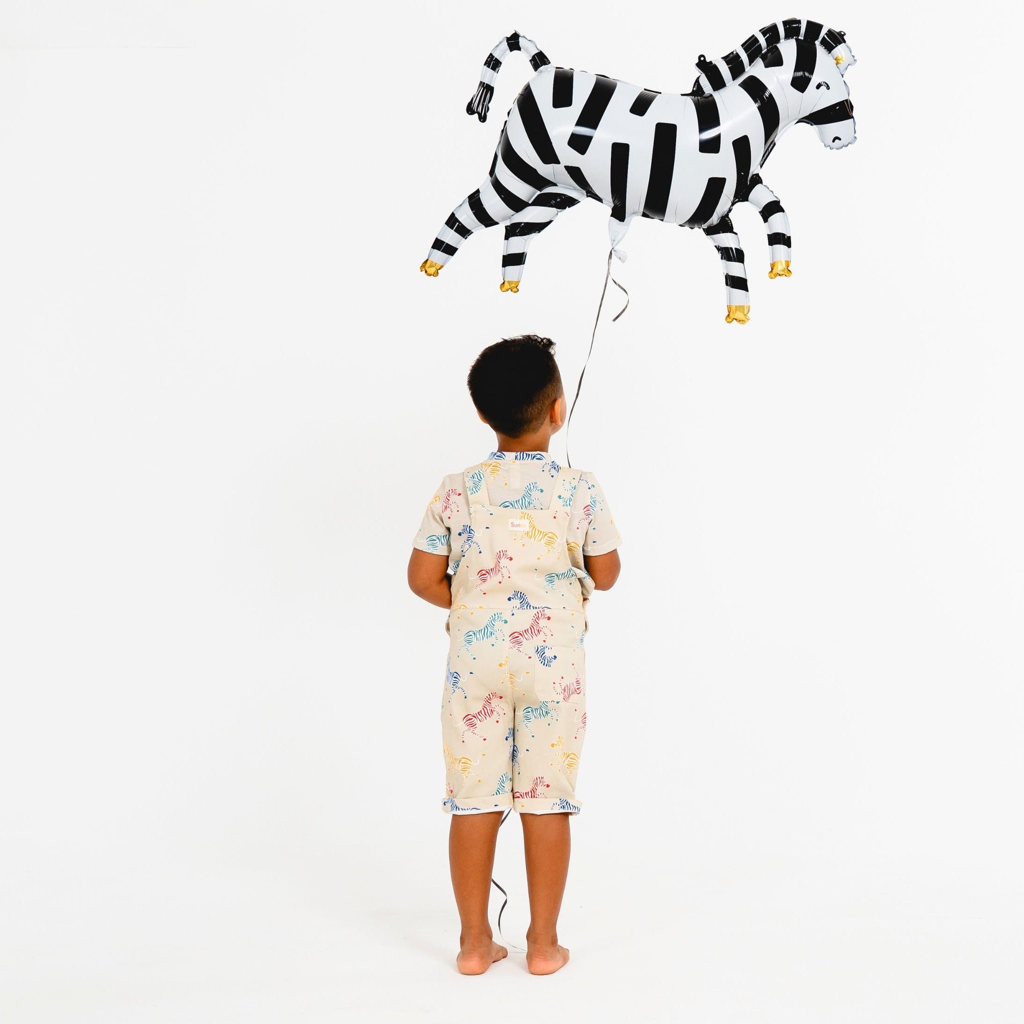 Back view of child holding a zebra balloon wearing zebra print shortarees by SunKin