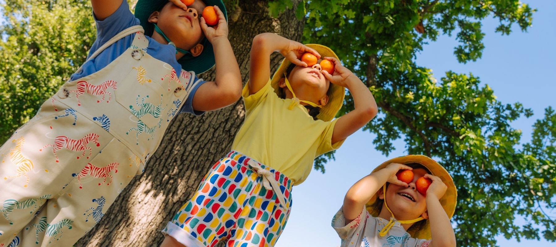 three children dressed in SunKin UV blocking clothes with clementines over their eyes