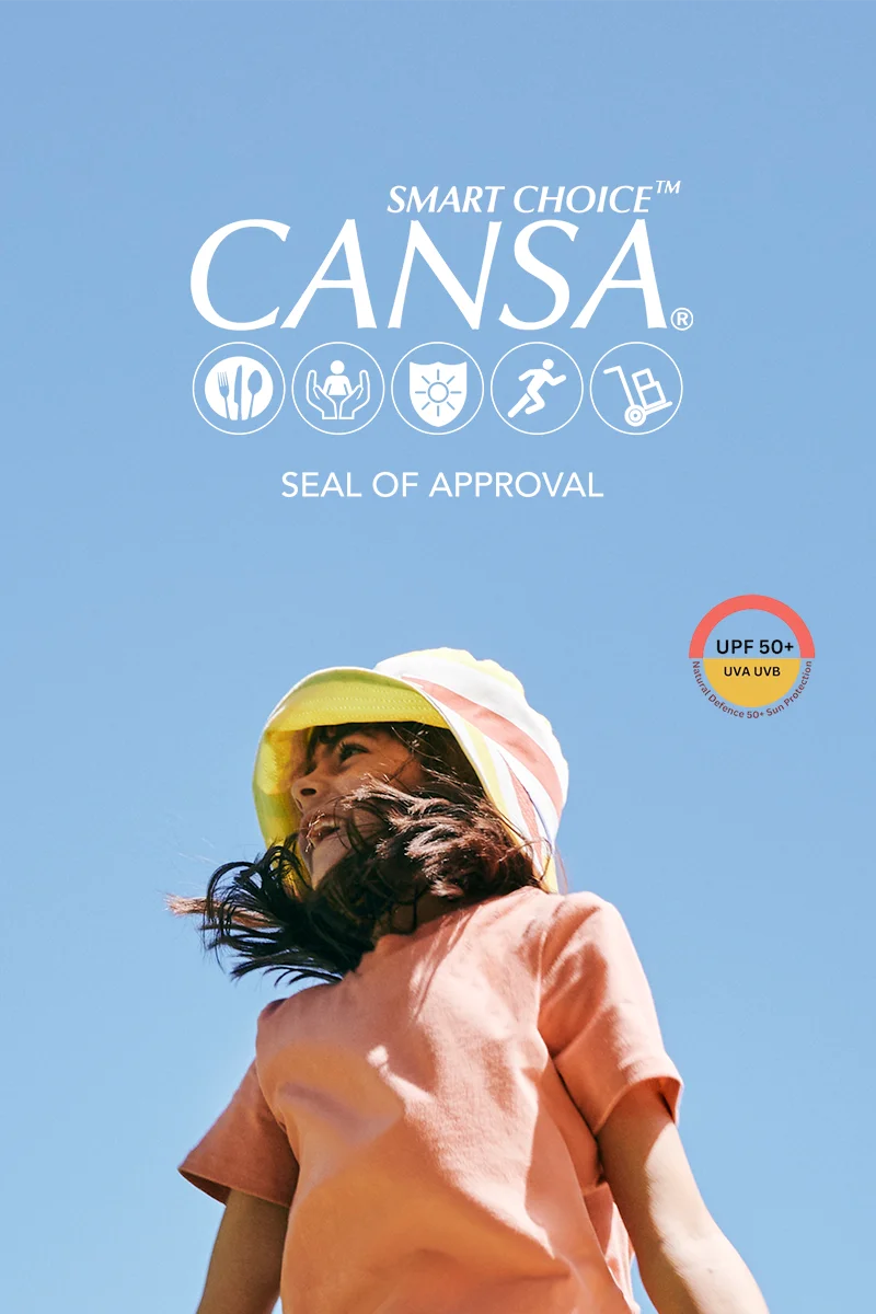 Child in UPF50+ SunKin clothing and wide-brim hat standing outdoors under blue sky with CANSA seal of approval displayed. MOBILE version