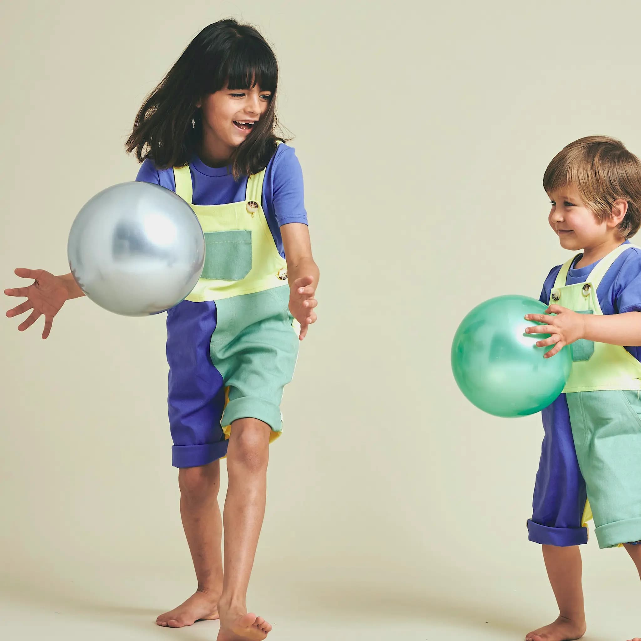Two children playing in SunKin’s UPF50+ multicolour shortarees—sun-smart, breathable cotton dungarees made for movement and matching joy.