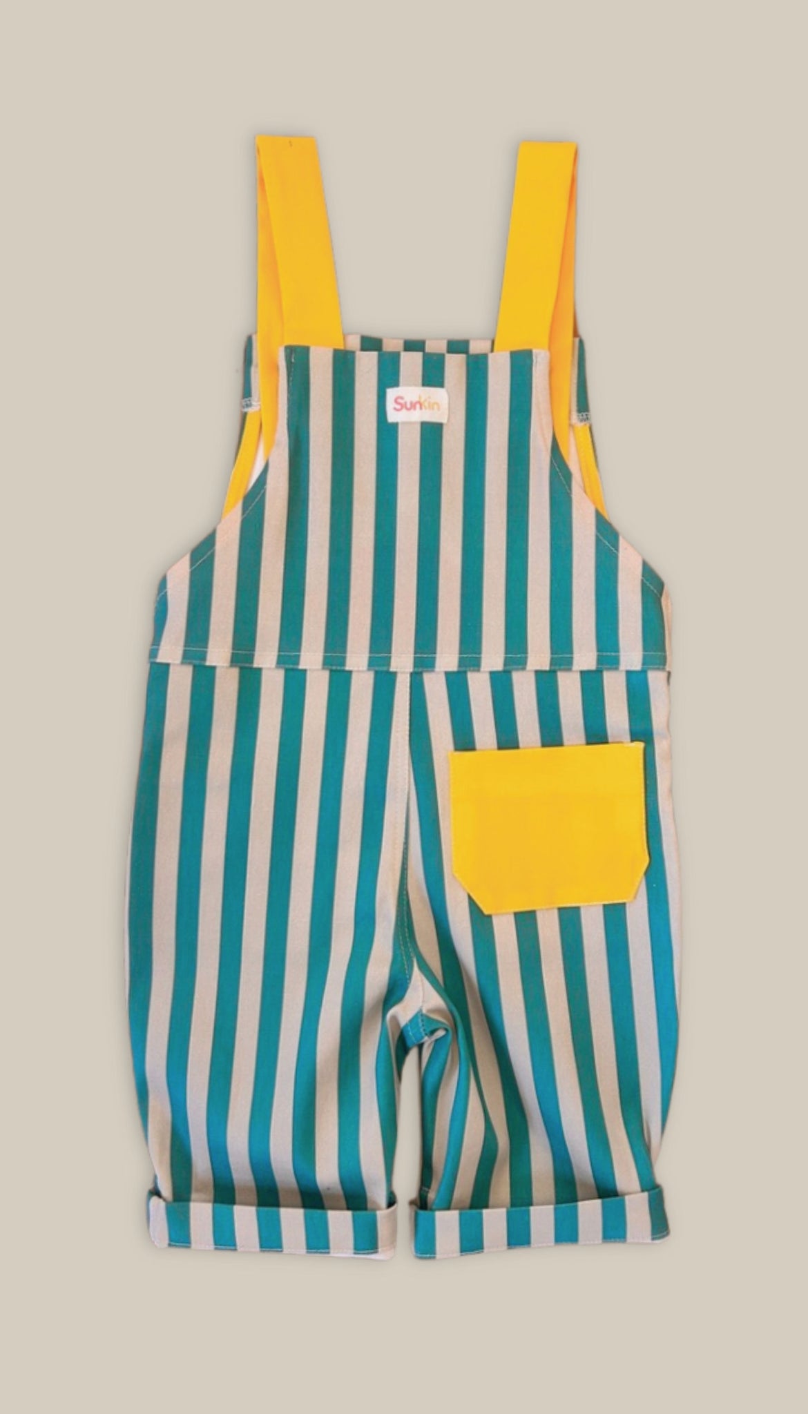 Back of striped overalls with yellow straps and pocket on a beige background